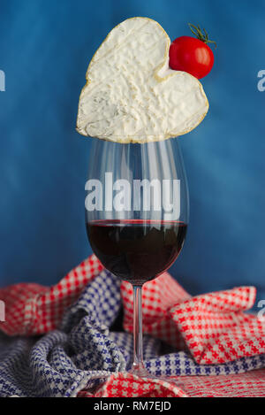 La composition avec Neufchatel, fromage normand (A.O.P.), verre de vin et la tomate cerise, sur fond bleu. Banque D'Images