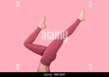 Femme tombe sur une montrant les jambes et leggings contre un fond rose Banque D'Images