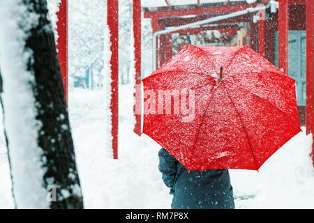 Triste et seule femme parapluie rouge sous la neige en hiver grâce à l'environnement urbain Banque D'Images