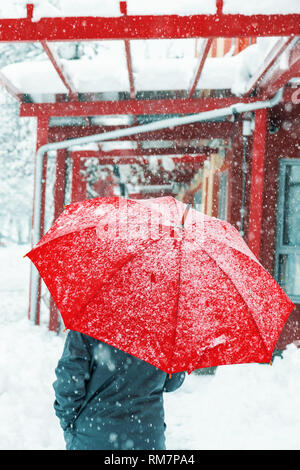 Triste et seule femme parapluie rouge sous la neige en hiver grâce à l'environnement urbain Banque D'Images