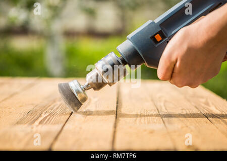 L'homme les mains avec brosse rotative électrique disque métal ponçage d'un morceau de bois Banque D'Images