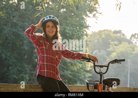 Mode de transport écologique en location. Belle jeune femme kasazy portant un casque bleu et cheveux longs pose debout à côté d'un orange-colore Banque D'Images