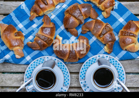 Deux tasses de café, des croissants avec du chocolat sur un tissu bleu et les planches de bois. Banque D'Images