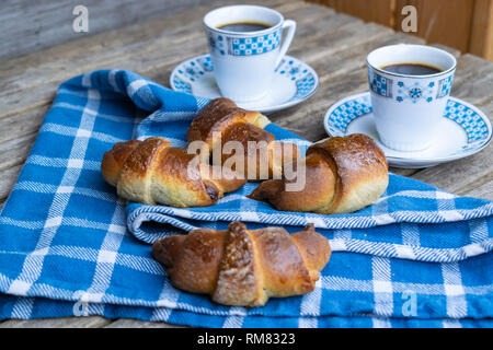 Deux tasses de café, des croissants avec du chocolat sur un tissu bleu et les planches de bois. Banque D'Images