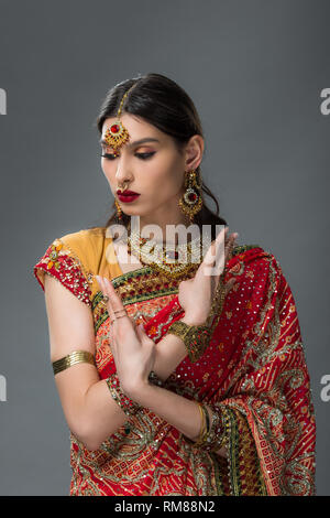 Belle femme indienne posant dans des vêtements traditionnels montrant mudra, isolé sur gris Banque D'Images