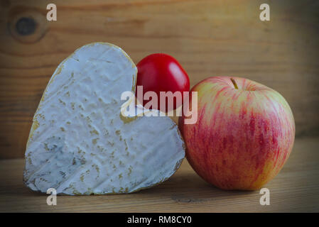 Nature morte avec un fromage Neufchatel (Norman A.O.P.) une tomate cerise et une pomme sur fond de bois Banque D'Images