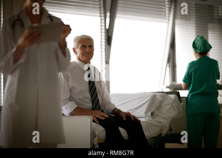 Vue d'un homme âgé assis sur un lit que deux médecins en veille. Banque D'Images