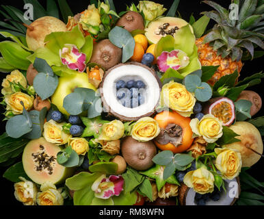 Boîte en bois avec plein de fruits exotiques et de fleurs isolé sur fond noir. Vue de dessus, close-up Banque D'Images