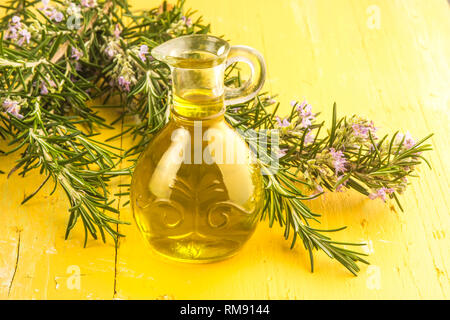 L'huile d'olive extra vierge aromatisée avec Rosemary sur table en bois jaune Banque D'Images