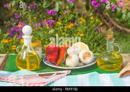 L'huile d'olive extra vierge en vintage deux pots en verre, l'ail, les poivrons, le romarin et la menthe sur l'ancienne table de jardin d'été Banque D'Images