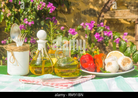 L'huile d'olive extra vierge dans deux bouteilles en verre vintage, ail, poivrons, romarin et menthe sur l'ancienne table de jardin d'été Banque D'Images
