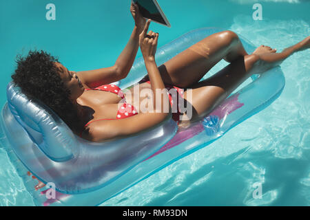 Young African American Woman relaxing on pool chaise longue et using digital tablet Banque D'Images