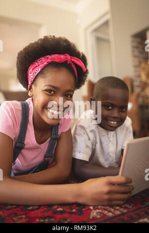 Happy African American sœur lying on floor with digital tablet and looking at camera Banque D'Images