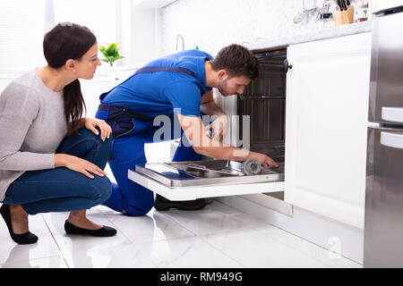 Jeune femme à la réparation de lave-vaisselle au réparateur dans la cuisine Banque D'Images