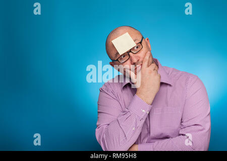 Un homme d'affaires dans un piked chemise a un post it sur le front, sur le fond bleu. Banque D'Images