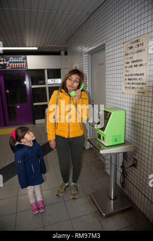 Femme au téléphone, mère avec fille au vieux téléphone vert, station de métro, Kyoto, Japon Banque D'Images