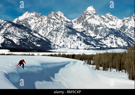 Une audacieuse jeune snowboarder sails off une étagère de neige immaculée en vue de l'impressionnante chaîne de montagnes Teton à Grand Teton National Park près de Jackson Hole, Wyoming, USA. Banque D'Images