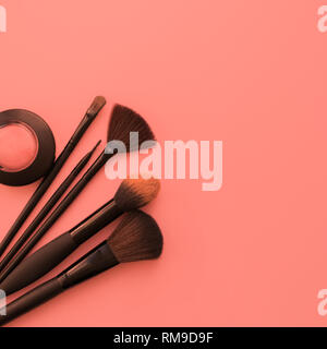 Différents Pinceaux de maquillage et une boîte de fard Ombre sur un fond corallien à la mode. Télévision mise en page. Concept de beauté. Banque D'Images