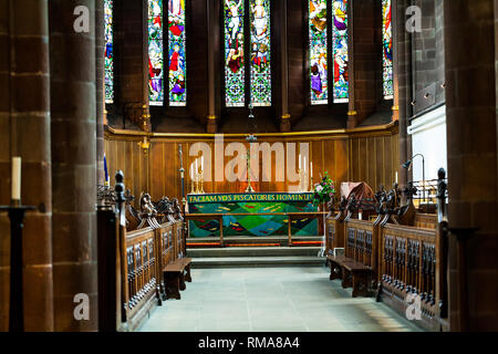 BIRMINGHAM, UK - Mars 2018 Vitrail derrière le Sanctuaire. Croix, bougie sur table d'autel et Lampe suspendue. Choir de bancs de chaque côté. Mini Sc Banque D'Images