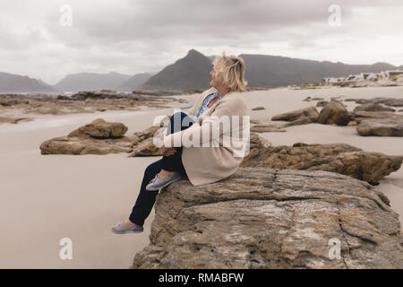Senior woman relaxing on the rock at beach Banque D'Images