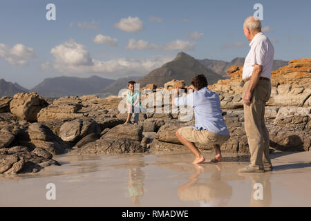 Père cliquant photo de son fils avec mobile phone on beach Banque D'Images