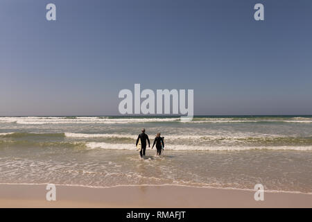 Surfer Senior couple en train de marcher ensemble sur la plage Banque D'Images