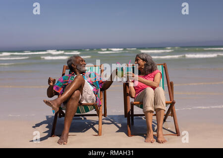 Couple de détente sur une chaise longue et le grillage verres à cocktail sur la plage Banque D'Images