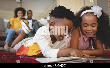Cute African American sœur couchée sur le plancher et la lecture d'un livre de contes Banque D'Images