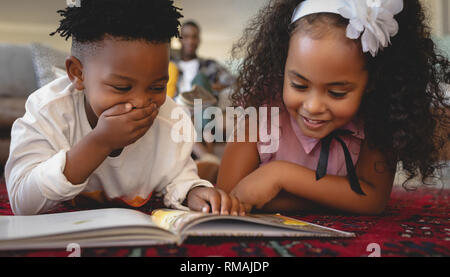 Cute African American sœur couchée sur le plancher et la lecture d'un livre de contes Banque D'Images