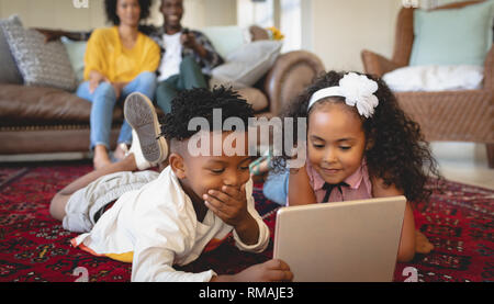 Cute African American sœur lying on floor and using digital tablet Banque D'Images