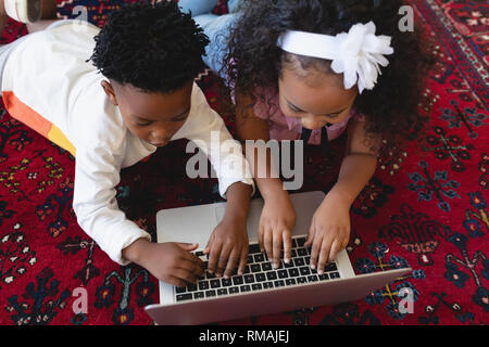 Cute African American sœur lying on floor and using laptop Banque D'Images