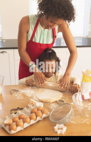 African American mother and daughter rolling out cookie dough in kitchen Banque D'Images