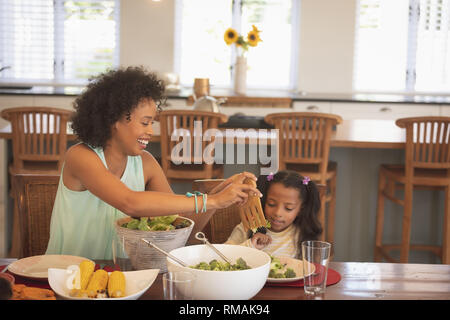 African American mother servant à sa fille salade à table à manger Banque D'Images