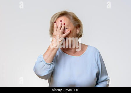 Senior woman couvrant son visage avec sa main alors qu'elle essaie de cacher ses émotions dans une vue en gros isolé sur gris clair Banque D'Images
