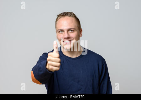 Positif souriant beau jeune homme donnant un coup de geste de succès et d'approbation sur un fond gris Banque D'Images
