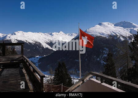 Haute-montagne couverte de neige, vue panoramique sur les collines et les pins, pont de bois. De brandir le drapeau rouge sur le vent. Ciel bleu clair, journée ensoleillée Banque D'Images