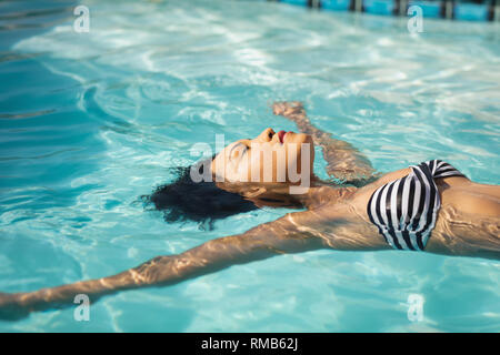 Les jeunes Métis woman floating in swimming pool Banque D'Images