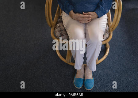 La section basse of senior woman with hand clasped sitting on chair Banque D'Images