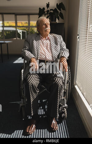 Vue avant de désactiver la haute homme assis sur fauteuil roulant et à l'extérieur à travers la vitre Banque D'Images