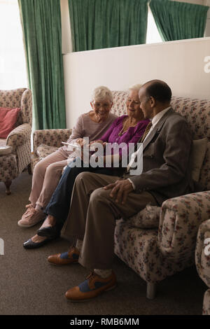 Vue avant du senior friends discussing over digital tablet while sitting on sofa Banque D'Images