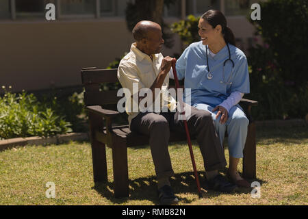 Vue avant du jeune femme médecin talking with senior homme pendant qu'assis sur un banc Banque D'Images