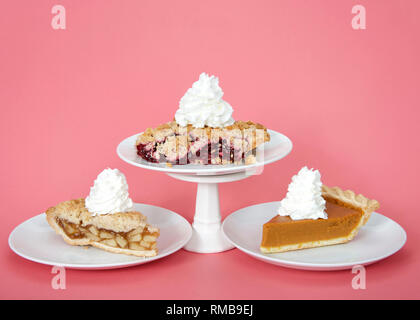 Apple et la citrouille sur plaques avec crème fouettée, cherry pie sur la plaque avec de la crème fouettée sur socle au-dessus d'eux. Fond rose. Journée nationale de pie m Banque D'Images