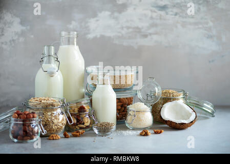 Bouteilles en verre de lait végétal vegan et amandes, noix, noix de coco, lait de graines de chanvre sur fond de béton gris. Bannière avec copie espace. Produits laitiers Lait subs Banque D'Images