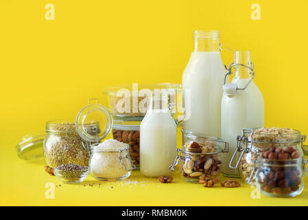 Bouteilles en verre de lait végétal vegan et amandes, noix, noix de coco, lait de graines de chanvre sur fond jaune. Bannière avec copie espace. Succédané de lait sans produits laitiers Banque D'Images