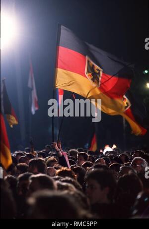 (03.10.1990) Berlin, à minuit, le noir-rouge-or drapeau est soulevée devant le Reichstag de Berlin comme un symbole de la réunification de la République fédérale et la RDA. Ici, les spectateurs applaudissent et vague avec l'Allemagne des drapeaux. Banque D'Images