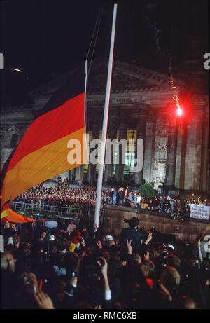 (03.10.1990) Berlin, à minuit, le noir-rouge-or drapeau est soulevée devant le Reichstag de Berlin comme un symbole de la réunification de la République fédérale et la RDA. Un spectateur a tiré une fusée flare. Banque D'Images