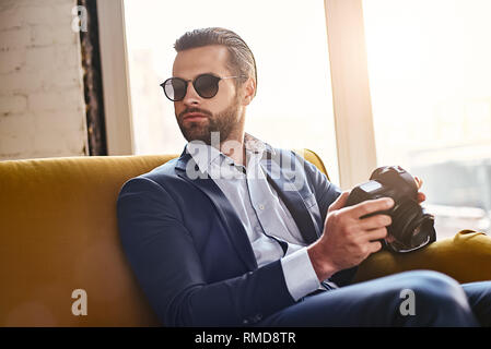 À la recherche d'inspiration. Jeune homme élégant avec succès dans les lunettes de soleil, appareil photo et est maintenant de penser à quelque chose. Style d'affaires. Regardez la mode Banque D'Images