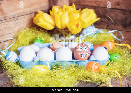 Composition de Pâques avec des oeufs blanc et brun en boîte avec un oeuf plâtré avec un drôle de visage. Banque D'Images