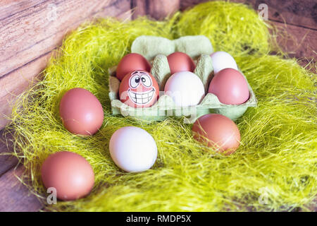 Composition de Pâques avec des oeufs blanc et brun en boîte avec un oeuf plâtré avec un drôle de visage. Banque D'Images