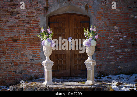 Des pots de fleurs décorés d'argile blanche avec un bouquet de printemps pastel d' hortensias positionnés de chaque côté d'une porte en bois vintage Banque D'Images